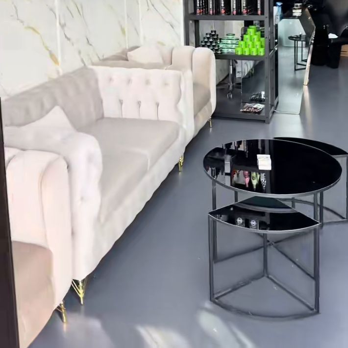 Wartebereich mit cremefarbenem Chesterfield-Sofa, schwarzen Glastischen und Produktregal vor einer Wand in Marmor-Optik